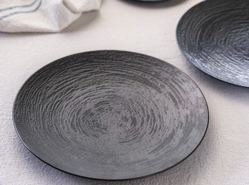 Two black ceramic plates on a light surface with a white cloth in the background.
